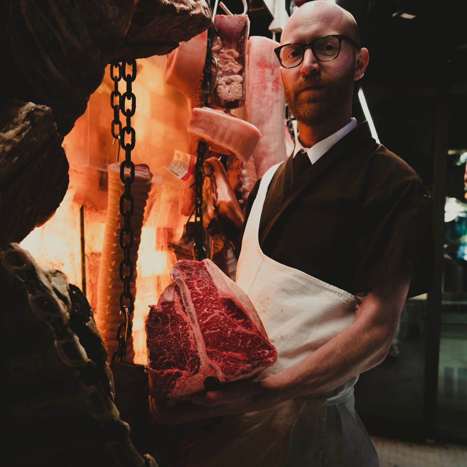 Boucher en tablier présentant une pièce de viande dans son atelier