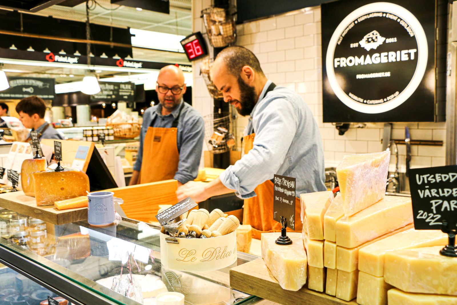 Fromagers au comptoir d'une crémerie, meules et tommes en vitrine