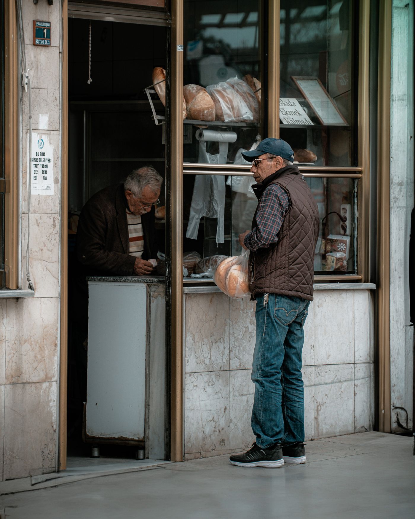 Client servi au guichet d'une boulangerie de quartier, pain à la main